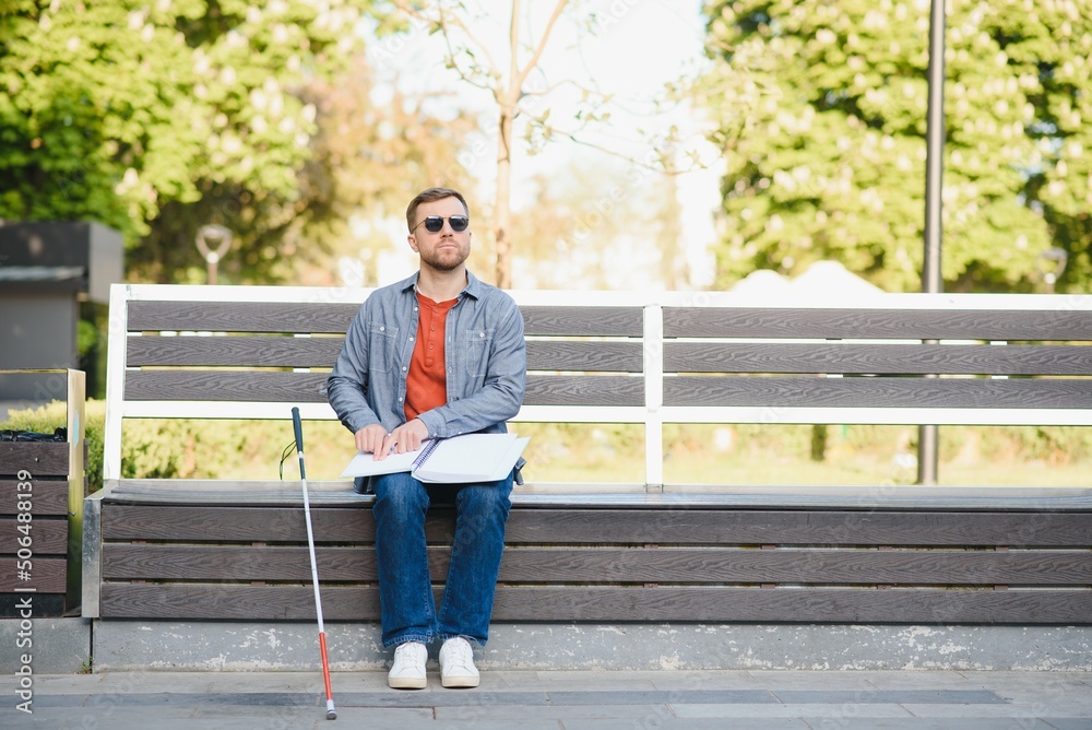 Blind man reading book on bench in park