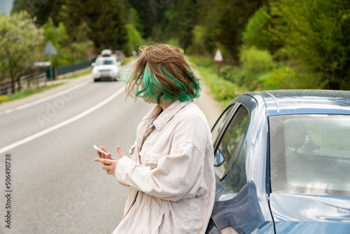 Caucasian hipster girl using a mobile phone to call the mechanic while looking at broken down car on street. Young girl with a broken car on the road call service. Cute girl near a broken car