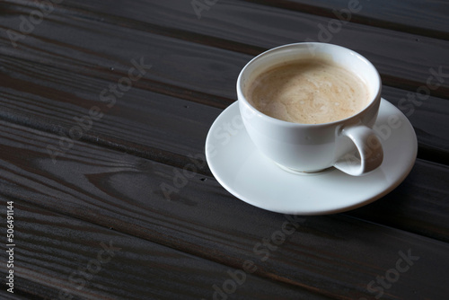 White cup with coffee on dark wooden table.