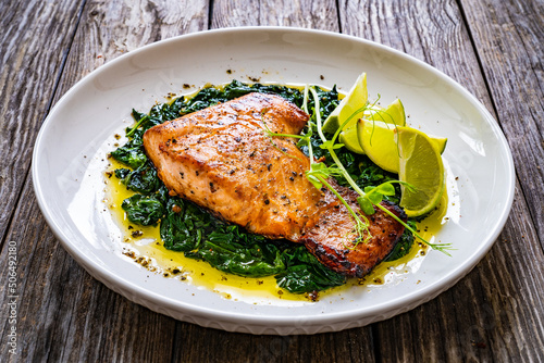 Fried salmon steak with spinach and lime served on wooden table 