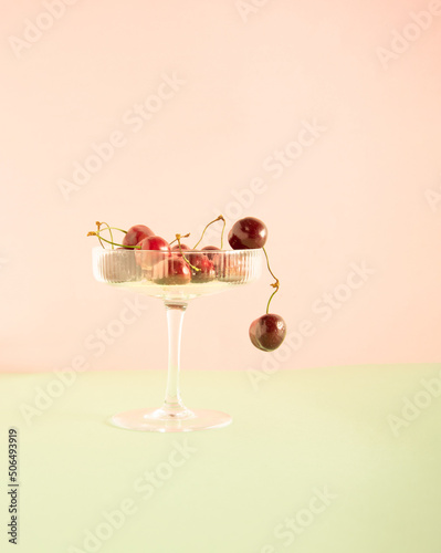 Art Deco champagne glass and cherry fruit, creative spring fruit arrangement against pastel pink background. 