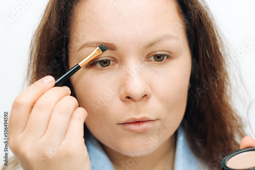 Girl with a brush paints eyebrows with dry shadows.