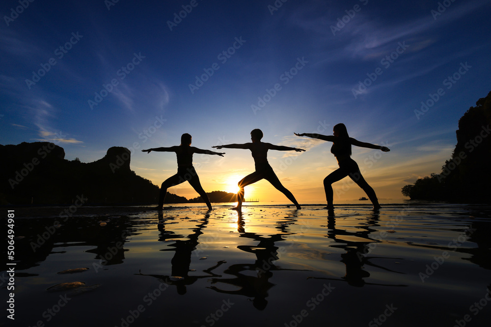 Women exercise Yoga on beach against beautiful sunrise or sunset