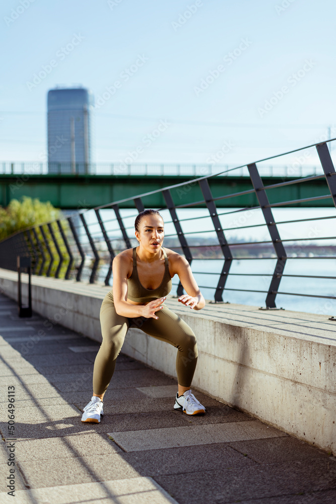 Fototapeta premium Young woman in sportswear exercising on a river promenade