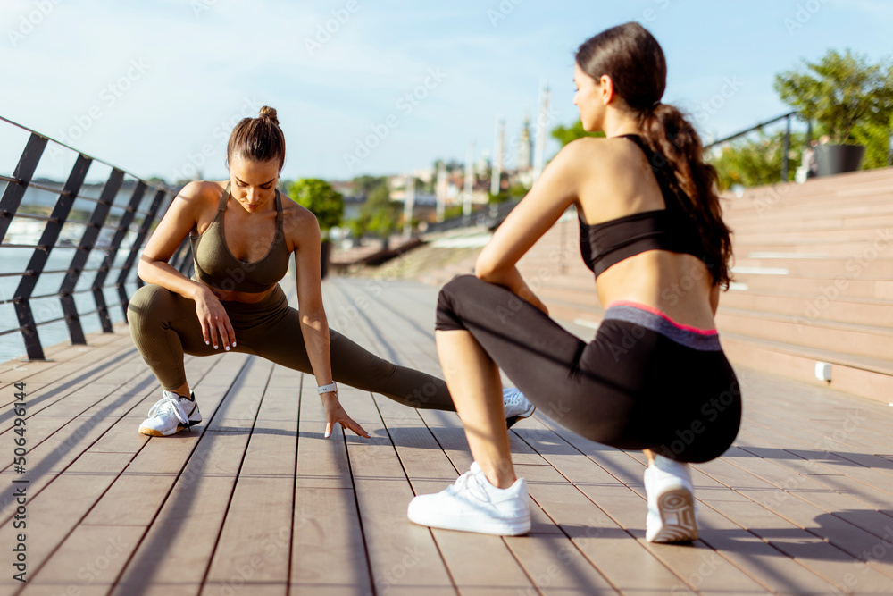 Obraz premium Young women in sportswear exercising on a river promenade