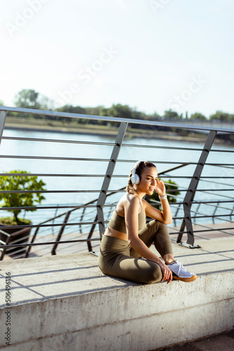 Pretty young woman with earphones takes a break after running in urban area