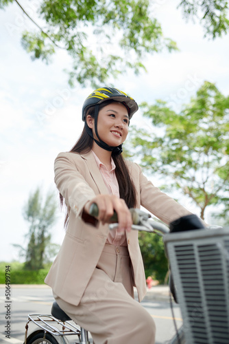 Smiling young Asian businessswoman in beige suit riding bicycle to office photo