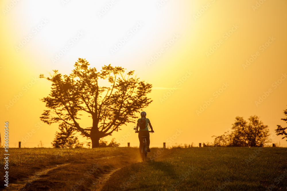 Female cyclist is riding a bicycle into the warm summer sunset Female cyclist is riding a bicycle into the warm summer sunset