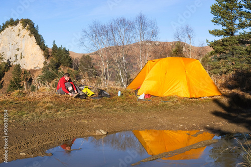Man traveler near a yellow tent in a tourist mountain camp. 