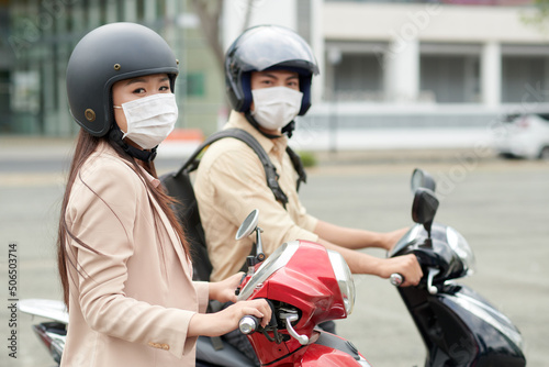 Asian young man and woman wearing medical masks and protective helmets when riding scooters in city