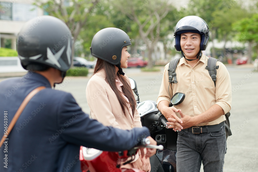 Fototapeta premium Positive coworkers in helmets talking after coming to work on scooters
