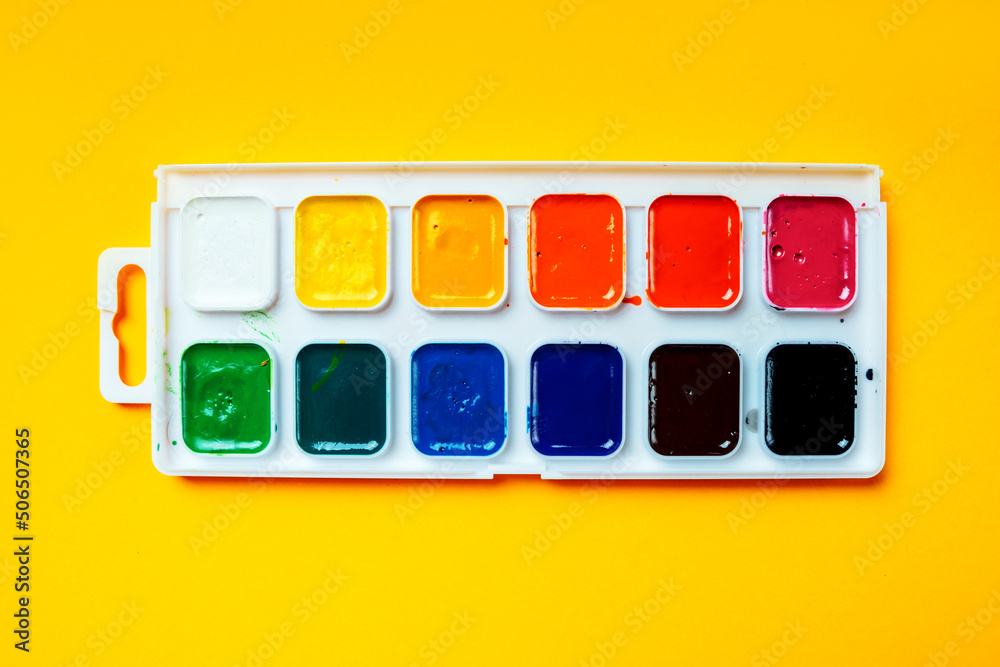 Palette with watercolor paints on a yellow background, top view.