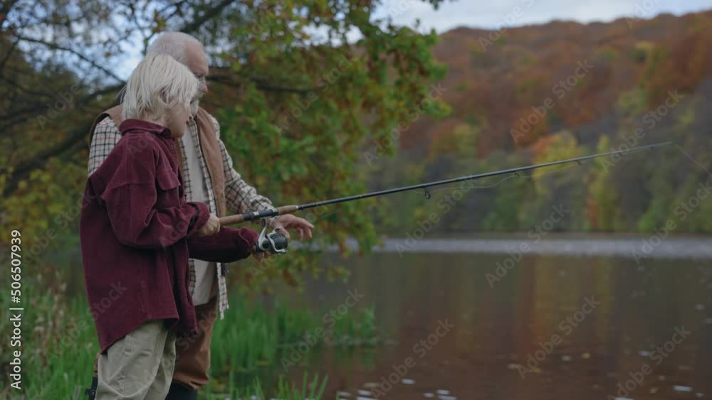 Boy holding fishing rod while standing with grandpa on lake Boy holding fishing rod while standing with grandpa on lake