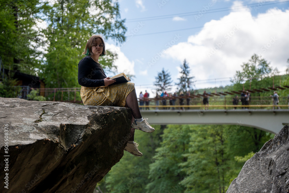 Young girl on a huge stone. Mountain stream in spring in the stony forest. Beautiful river flowing by the forest during the Spring. Carpathian, Ukraine spring forest creek. Long exposure Young girl on a huge stone. Mountain stream in spring in the stony forest. Beautiful river flowing by the forest during the Spring. Carpathian, Ukraine spring forest creek. Long exposure