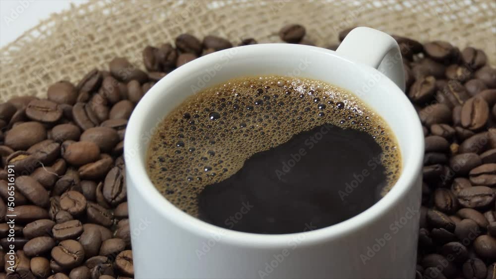 White cup with coffee on the background of fresh roasted coffee beans White cup with coffee on the background of fresh roasted coffee beans