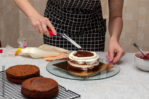 Woman's hand with kitchen spatula smoothes the caramel filling in the cake. Selective focus. Picture for articles about food, confectioners.