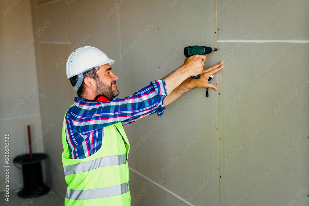 Construction worker using battery drill on building site.