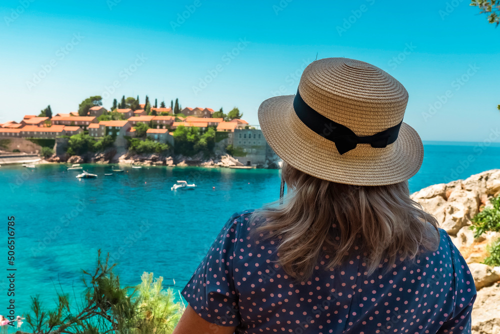 Montenegro. Adriatic Sea. Island and beach of Sveti Stefan. Summer. Sunny weather. A very popular tourist spot. Woman in a straw hat admiring the beautiful view