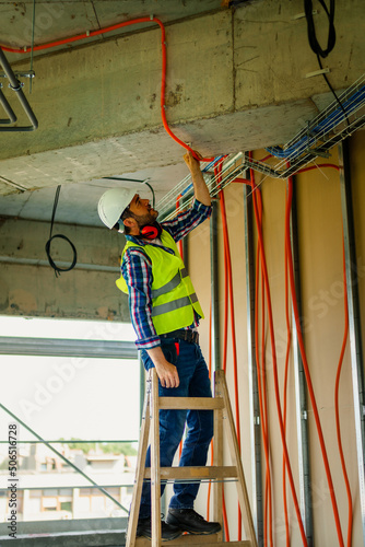 An experienced electrician who stands on a ladder and adjusts cable bellows for the electrical network of the building where he works.