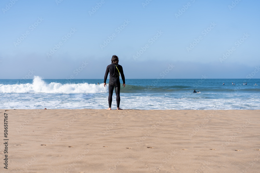One man dressed black wetsuit standing ocean beach rear view looking on horizon