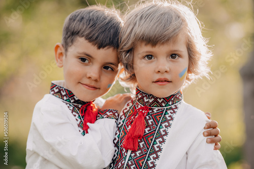 Smiling little ukrainian boys with blue yellow flag art on cheeks. Children together in traditional embroidery vyshyvanka shirts. Ukraine, brothers, freedom, national costume, victory in war. photo