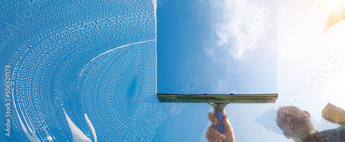 Window cleaner cleaning window with squeegee and wiper on a sunny day with a bright blue sky photo