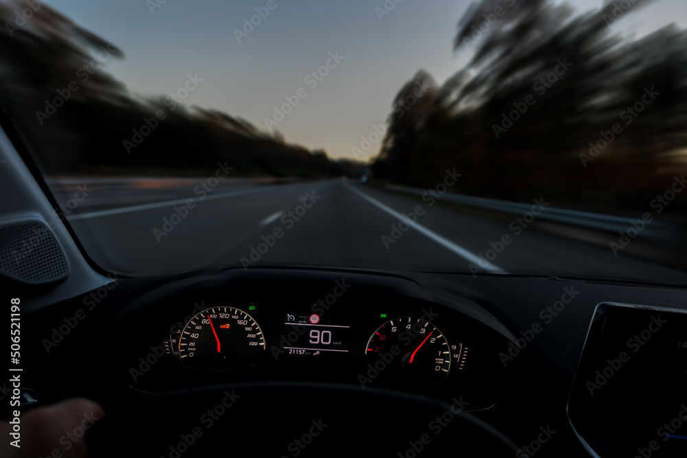 Driver view to the speedometer and the road blurred in motion, night fall view from inside a car of driver POV of the road landscape.