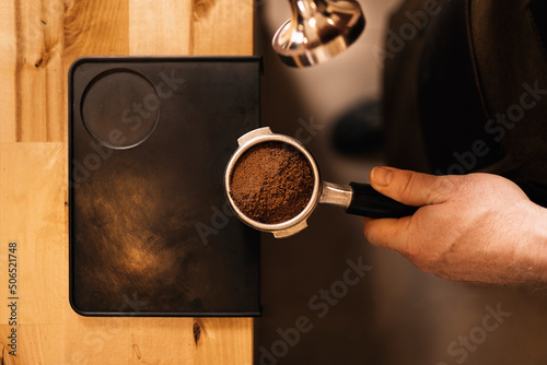Crop anonymous man using tamper for pressing ground coffee in portafilter