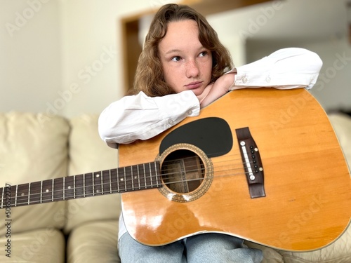 sad fair-haired girl sits with a guitar she thought she is dressed in a white blouse and blue jeans. High quality photo