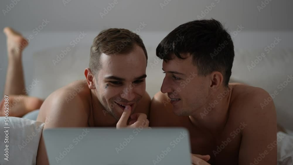 Front view relaxed gay couple cuddling watching film online on laptop smiling. Happy loving Caucasian LGBTQ men hugging lying on bed at home indoors enjoying leisure Front view relaxed gay couple cuddling watching film online on laptop smiling. Happy loving Caucasian LGBTQ men hugging lying on bed at home indoors enjoying leisure