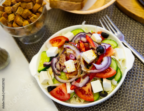 Traditional Greek salad with fresh vegetables, feta cheese and black olives served on white plate.