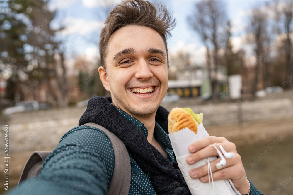 One man standing outdoor in autumn spring or winter day holding sandwich  tourist wearing shirt eating