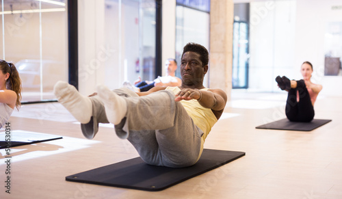 Fotografia Portrait of sporty aframerican man doing stretching workout during group pilates training at gym