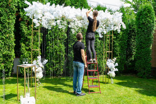 Woman and man decorate the wedding photo area with white flowers on a green lawn photo