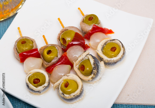 Piquant tapa of marinated anchovies fillet rolls with stuffed olives, onion and paprika on skewers photo