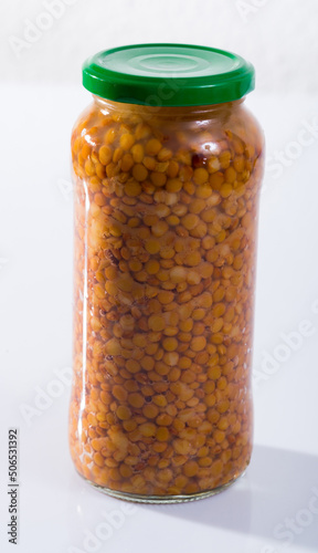 Glass jar with cooked lentils on white surface. Organic products for healthy eating.