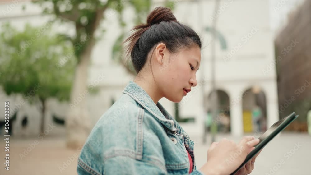 Side view shot of attractive Asian student reading lecture on digital tablet sitting on bench at the college campus. Online study concept Side view shot of attractive Asian student reading lecture on digital tablet sitting on bench at the college campus. Online study concept