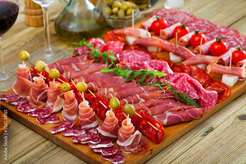 Cold cuts from Spanish ham, spicy dry-cured sausages and bacon with olives, cherry tomatoes and arugula on wooden plate