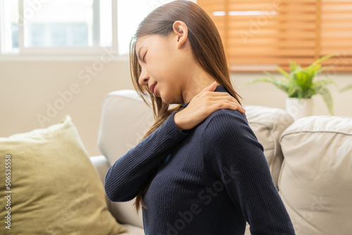 Body muscles stiff problem, asian young attractive woman, girl pain with back pain ache from work, holding massaging rubbing shoulder hurt or sore, painful sitting on sofa at home. Healthcare people.
