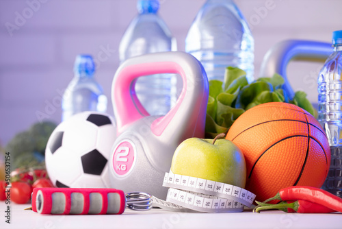 Fitness concept. Healthy nutrition: fruits and vegetables. Equipment for fitness exercises: weighing machine and dumbells on wooden wwhite table.
