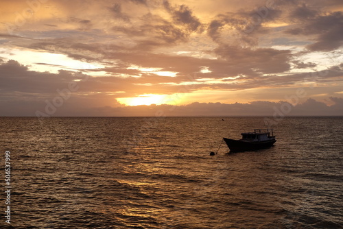 Sunset view with silhouette of fishing boats in the ocean. Warm colored sky with beautiful clouds.