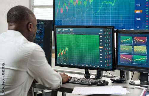 Unrecognizable Black man sitting at desk in office reuploading page with current stock trading stats