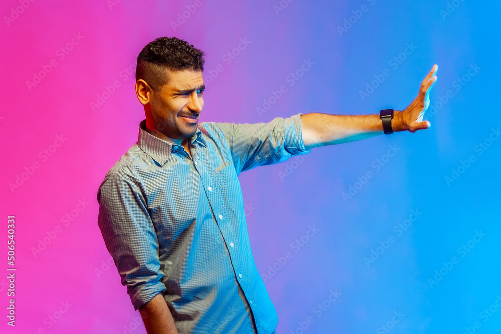 Side view of man in shirt making stop gesture showing palm of hand, conflict prohibition warning about danger, stop bullying. Indoor studio shot isolated on colorful neon light background.