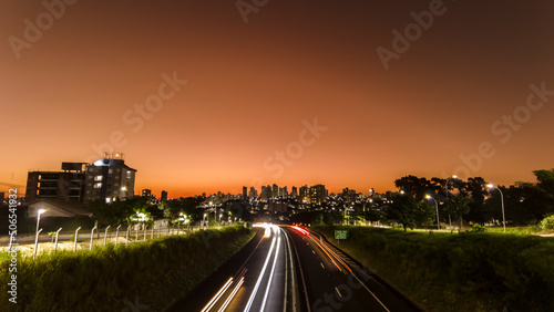 Fototapeta Naklejka Na Ścianę i Meble -  Trail of light caused by vehicular traffic in SP-294, Comandante Joao Ribeiro Barros Highway with buildings from downtown in the background, in Marília,