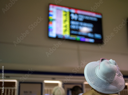 Принти на полотні An attendee at a horse race, wearing a fancy hat before placing a wager