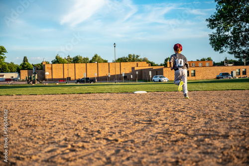 Male youth running bases after hitting the baseball.
