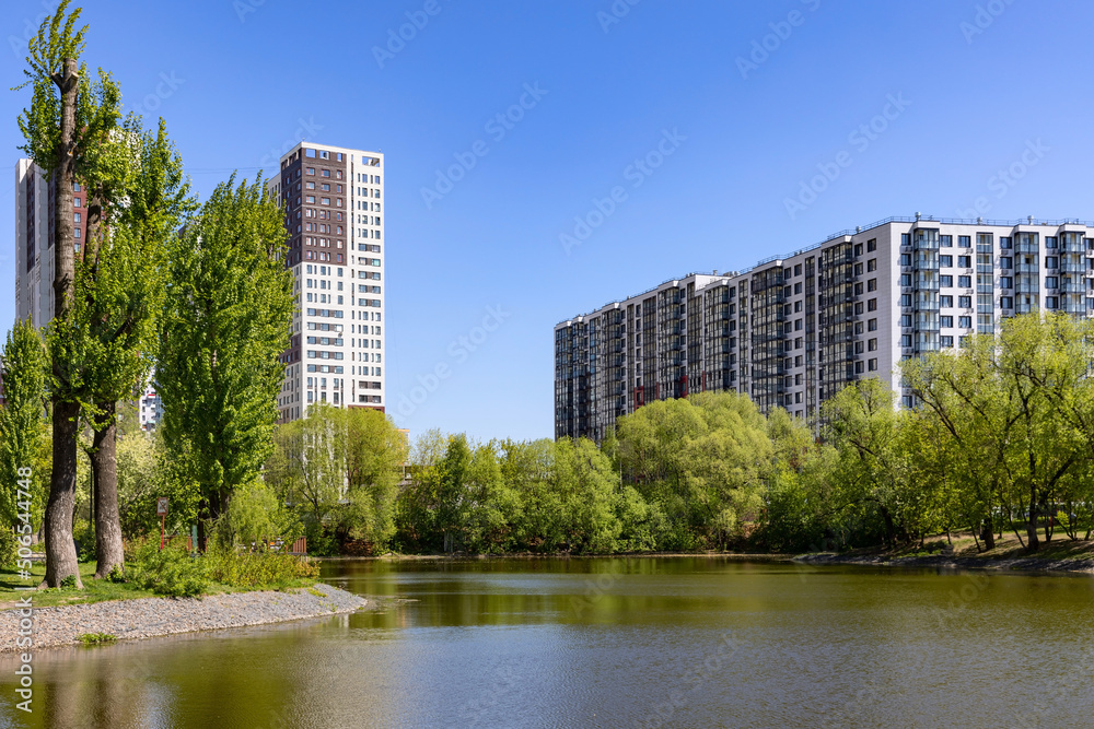 New modern residential district with apartment buildings near the lake surrounded by green trees park