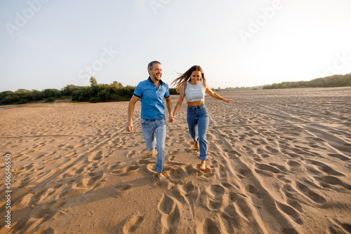 Happy young couple in love is having fun on a wild beach, running towards the sun. Rest, youth, love, lifestyle, solitude with nature.