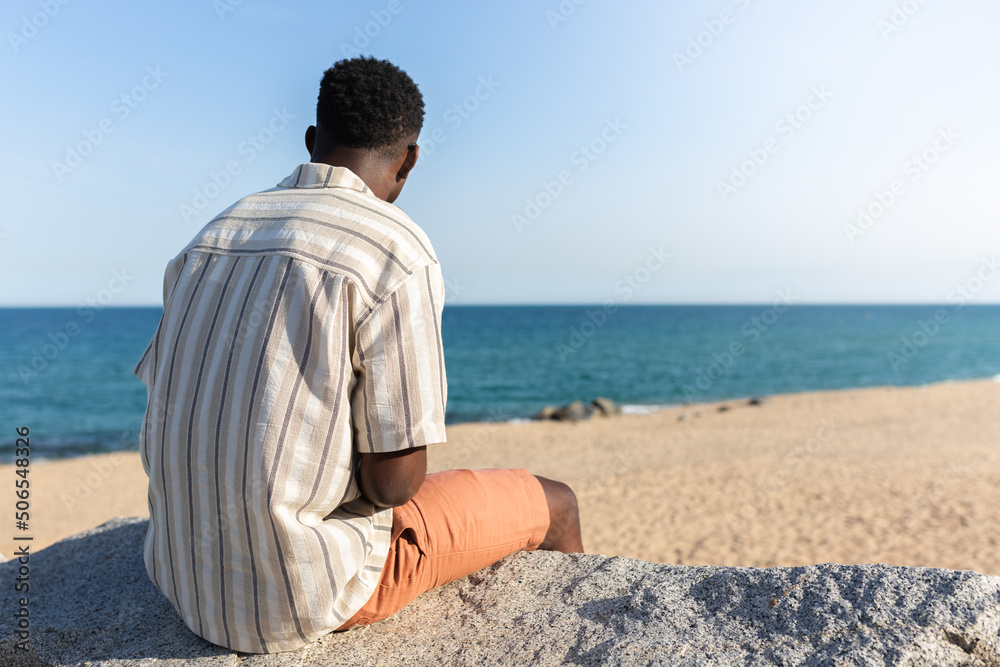 Back view of black man relaxing looking at the ocean. Copy space.