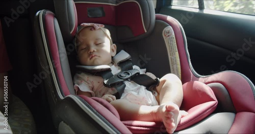 Happy Asian baby sleeping in car seat next to mother during family road trip. Toddler safe and comfortable car travel. Asia law enforcement for passenger safety product concept.
